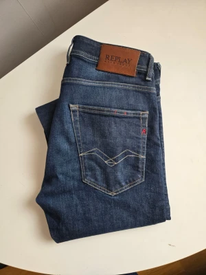 Mörkblå jeans från Replay - Snygga mörkblå jeans från Replay med klassisk femficksmodell och kontrastsömmar. Jeansen har en rak passform och detaljer som läderpatch med logga bak samt diskreta slitningar framtill. Perfekta för en trendig och avslappnad stil.
