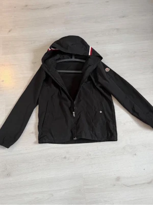 Moncler jacka  - Moncler windbreaker i svart , bra skicka bara att en knapp har lossnat från fickan men annars fint skick, passar lite olika står storlek 4 så de är undergår M/L passar de, pris inte hugget i sten! Hör av 