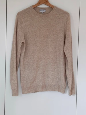 Beige stickad tröja från Davida (S) - Mysig beige stickad tröja från Davida i klassisk modell med rund halsringning och långa ärmar. Tillverkad i mjukt material (Cashmere) som ger en avslappnad och stilren look. Perfekt för lager på lager under kyliga dagar.