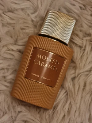 Molten Caramel parfym Paris Corner - Molten Caramel parfym från Paris Corner i en snygg brun flaska med räfflad yta och guldfärgat lock. Flaskan har en elegant metallisk etikett framtill och ger ett lyxigt intryck. Perfekt för dig som gillar söta och karamelliga dofter.
