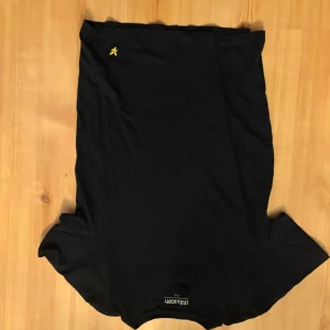 Svart t-shirt från Lyle & Scott - Snygg svart t-shirt från Lyle & Scott med klassisk gul logga broderad på bröstet. T-shirten har rund hals och korta ärmar, tillverkad i mjukt bomullsmaterial som känns skönt mot huden. Perfekt basplagg för en clean och stilren look.