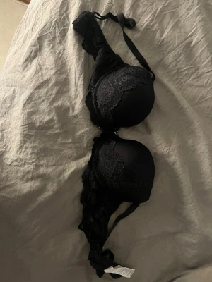 Svart bh med spetsdetaljer - Snygg svart bh med vadderade kupor och fina spetsdetaljer längs kanterna. Axelbanden är justerbara och bh:n har hakknäppning bak. Materialet är en mix av mjuk textil och spets som ger en elegant look.