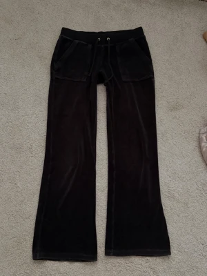 Juicy Couture byxor  - Mörksvarta mjukisbyxor i mjuk velour med breda ben och dragsko i midjan. Byxorna har stora fickor fram och bak, bakfickorna har knappdetaljer. Perfekta för chill dagar och riktigt sköna att ha på sig.