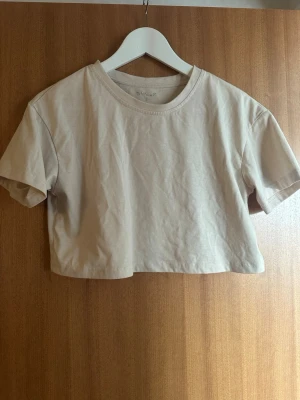 Beige croppad t-shirt från SHEIN - Säljer en enkel och stilren beige croppad t-shirt från SHEIN. T-shirten har rund halsringning och korta ärmar, perfekt till sommaren. Tillverkad i mjuk bomull för en skön känsla. Matcha med jeans eller kjol för en clean look.