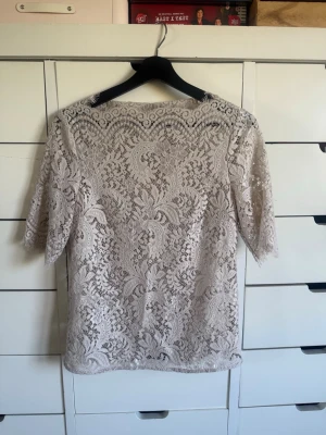 Beige spetsblus med halvärm - Säljer en superfin beige spetsblus med halvärm och rund hals. Blusen är helt genombruten med ett detaljerat spetsmönster och har en feminin, elegant look. Perfekt att styla med jeans eller kjol för en trendig outfit.