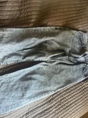 Grå tvättade raka jeans - Säljer ett par grå tvättade jeans med rak passform och klassisk femficksdesign. Jeansen har en snygg vintage look och är tillverkade i denim. Perfekta för dig som gillar en avslappnad och trendig stil.