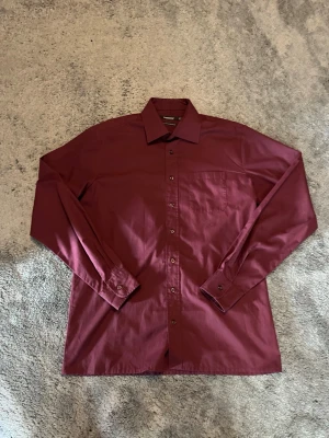 Vinröd skjorta från Dressmann  - Snygg vinröd skjorta från Dressmann i storlek M. Skjortan har klassisk krage, bröstficka och knäppning framtill. Tillverkad i en lättskött bomullsblandning som känns bekväm hela dagen.  Aldrig använd! Skriv om du har funderingar😇