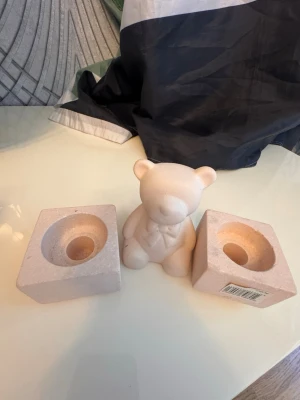 Ljuslyktor och dekoration björn - Två ljuslyktor i beige stenmaterial, fyrkantiga med rund öppning för värmeljus, mått 5,5x5,5x4,5 cm. Medföljer en söt björnfigur i liknande färg och material, perfekt som dekoration till hemmet.