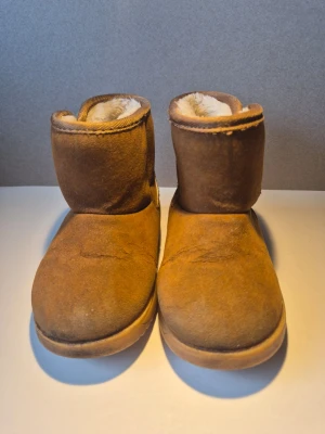 Bruna moon boots med foder barnskor - Mysiga bruna moon boots med mjukt vitt foder på insidan. Skorna har en klassisk rund tå och är tillverkade i mockaliknande material. Perfekta för kalla dagar när du vill hålla fötterna varma och bekväma.