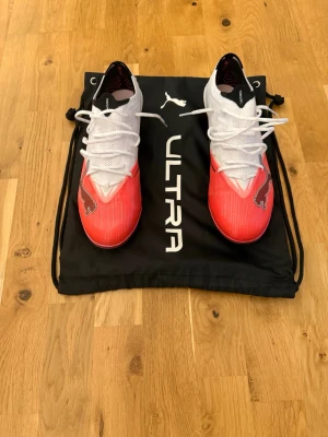 PUMA ULTRA NITRO 7 ULTIMATE AG THE ARRIVAL - ULTRA RED/PUMA SVART/PUMA WHITE - Säljer ett par snygga Puma Ultra fotbollsskor i vitt och rött med svarta detaljer. Använda 2 gånger endast Skorna har en låg profil, snörning och lätta material för maxad fart på planen. Sulan har fasta dobbar för bra grepp på gräs. Perfekta för dig som vill sticka ut på matchen!