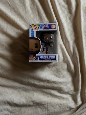 Funko Pop LeBron James Space Jam - Cool Funko Pop-figur av LeBron James från filmen Space Jam: A New Legacy. Figuren är i klassisk Funko-stil med stort huvud och detaljerad basketoutfit i blått och rött. Kommer i originalförpackning med fönster. Perfekt för samlare eller fans av Space Jam.