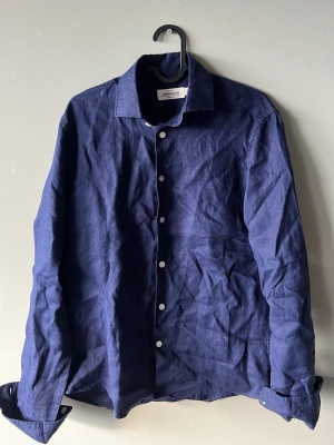 Linneskjorta - Stilren mörkblå skjorta i linne med klassisk krage och vita knappar framtill. Skjortan har lång ärm och en avslappnad passform, perfekt för en trendig och bekväm look. Storlek Xs aldrig Andvänd bara testad 