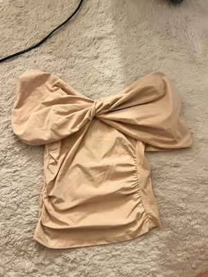 Beige axelbandslös topp med rosett - Supersnygg beige axelbandslös topp med stor rosettdetalj framtill. Aldrig använd 🥰