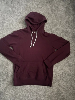 Vinröd pier one hoddie - Säljer en vinröd hoodie med klassisk huva och vita dragsnören. Hoodien har en stor magficka och ribbade muddar vid ärmar och nederkant. Perfekt för en avslappnad stil och enkel att matcha med jeans eller joggers.