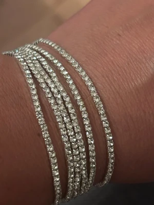 Silverfärgat armband med strasspärlor - Snyggt armband i silverfärg med flera tunna rader av glittrande strasspärlor. Armbandet har en elegant och modern design som ger en lyxig känsla. Perfekt för dig som vill ha något som sticker ut och glänser lite extra. Kan träffa i Göteborg 
