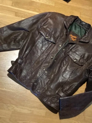 Mörkbrun vintage skinnjacka - Säljer en mörkbrun skinnjacka med klassisk retrostil. Perfekt för dig som gillar tidlös och edgy look. 