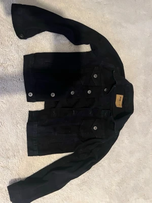 Svart jeansjacka med silverknappar - Stilren svart jeansjacka med klassisk rak passform och silverfärgade knappar framtill. Storlek XS