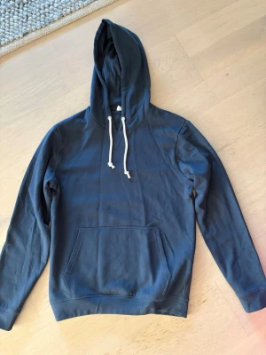 Mörkblå hoodie från pier one - Aldrig använd!!!!!! En enkel och stilren mörkblå hoodie från pier one med stor känguruficka framtill och vita dragsnören i huvan. Hoodien har långa ärmar och ribbade muddar vid ärmslut och nederkant. Perfekt för en avslappnad och grischl look. Be gärna om fler bilder så löser jag det!