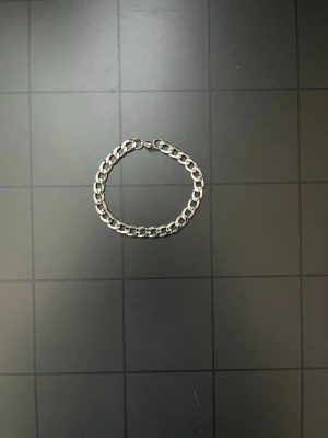 Kedjearmband i silverfärg - Snyggt armband i silverfärgad metall med breda, platta länkar och karbinlås. Perfekt för dig som gillar en stilren och enkel accessoar. Passar till många olika outfits och ger en cool touch till din stil.