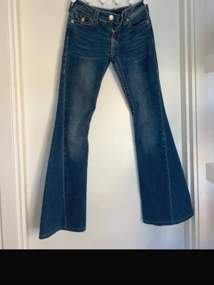 True Religion jeans  - Säljer ett par blå bootcut True religion jeans med utsvängda ben och klassiska fem fickor. Jeansen har en snygg tvätt och kontrastsömmar. Dessa är knappt använda och är precis som nya! 