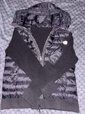 Svart moncler cardigan - Snygg svart moncler cardigan med quiltat mönster, huva och ribbstickade ärmar samt muddar. Jackan har dragkedja framtill och två fickor. Om ni har frågor så är de bara att fråga🤗