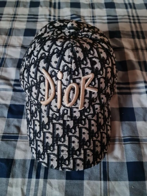 Mönstrad keps från Dior - Säljer en snygg keps från Dior med klassiskt monogrammönster i svart och beige. Kepsen har broderad Dior-logga framtill och på sidan. Materialet är tyg med struktur och kepsen har böjd skärm. Perfekt för dig som gillar exklusiva accessoarer.