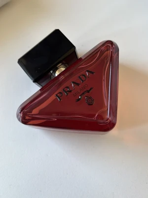 Prada röd trekantig parfymflaska - Snygg parfym från Prada i en unik trekantig flaska av rött glas med svart lock. Flaskan har tydlig Prada-logga och Milano-tryck på framsidan. Perfekt som statement på parfymhyllan och ger en lyxig känsla till din samling. kommer med förpackningen, aldrig använt ❤️