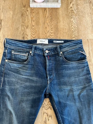 Blå jeans från Replay - Snygga blå jeans från Replay med klassisk femficksmodell och kontrastsömmar. Jeansen har en mörk tvätt och detaljer som läderpatch bak i midjan samt broderad bakficka. Perfekta för en avslappnad och trendig look. Har används, men fortfarande väldigt fint skick på dom! Bara att höra av sig om man vill ha fler bilder