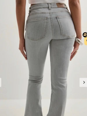 Ljusgrå bootcut jeans - Snygga ljusgrå jeans med bootcut passform och hög midja. Jeansen har klassiska fem fickor och bälteshällor. Tillverkade i stretchigt denimtyg för en bekväm känsla och en smickrande siluett. Perfekta för en trendig och avslappnad look.