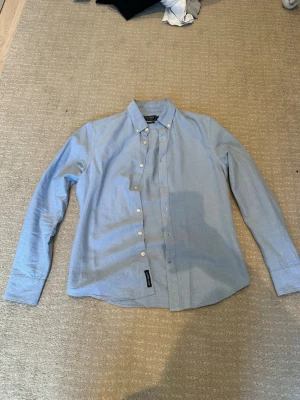 Ljusblå skjorta från East West 100% bomull storlek S - Säljer en ljusblå skjorta från East West i slim fit-modell. Sjukt bra att bara ha på dig eller under tex en kavaj, inget fel knappt använd, slå en singlar vid intresse eller något liknande!