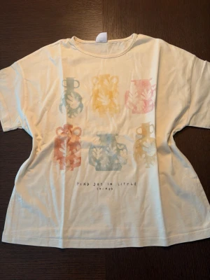 Vit t-shirt med färgglada vaser - Vit t-shirt med tryck av sex färgglada vaser i pastellfärger och texten 'Find joy in little things' framtill. T-shirten har rund hals och korta ärmar. Perfekt för dig som gillar konstnärliga och unika motiv.