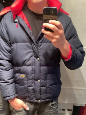 Mörkblå pufferjacka med röd huva - Säljer en marinblå dunjacka från polo Ralph lauren. Perfekt för kalla vinterdagar och en stilren look. Storlek är 14-16 men den är ganska stor så skulle säga att den passar i xs. Modellen är 170cm och väger 64kg. Priset är inte skrivet i sten och kan ändrar vid en snabb affär😁