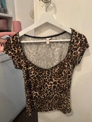 Leopardmönstrad topp med kort ärm - Säljer en snygg leopardmönstrad topp med korta ärmar och djup rundringning. Toppen har en figurnära passform och är tillverkad i ett mjukt, stretchigt material som känns bekvämt mot huden. Perfekt för dig som vill sticka ut med ett djuriskt print.