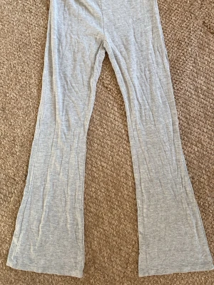 Grå mjukisbyxor med utsvängda ben - Säljer ett par ljusgrå mjukisbyxor med utsvängda ben. Byxorna har resår i midjan och är gjorda i ett mjukt och stretchigt material, perfekt för chill dagar. Passar dig som gillar en relaxed och trendig stil. Från lager 157