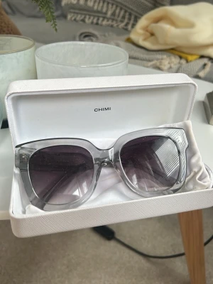 Grå transparenta solglasögon CHIMI 08 - Snygga solglasögon från CHIMI med transparent grå båge och stora, fyrkantiga glas. Glasen är mörktonade och ger en cool look. Kommer i originaletui. Säljs då de ej kommer till användning, bara använda ett fåtal gånger och köpta i chimis butik. 