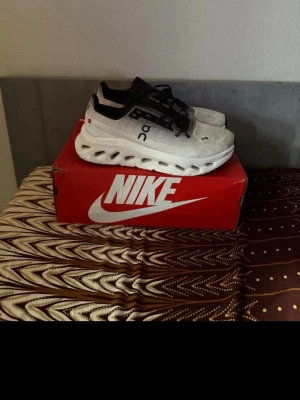 Vita On sneakers med svart detalj - Säljer ett par vita sneakers från On med svarta detaljer och unika hålmönstrade sulor. Skorna har snörning och en sportig, modern look. Perfekta för dig som gillar stilrena och bekväma sneakers.