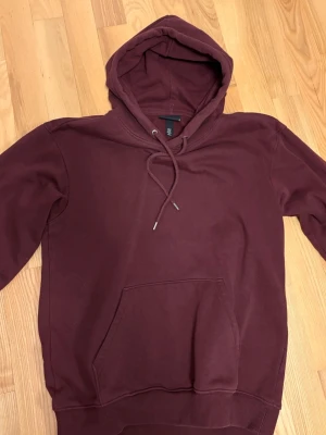 Vinröd hoodie från H&M Loose Fit - Snygg vinröd hoodie från H&M i loose fit-modell. Hoodien har en stor huva med dragsko, magficka och ribbade muddar vid ärmslut och nederkant. Perfekt för en chill och avslappnad stil. Materialet är mjukt och skönt, troligtvis bomullsblandning.