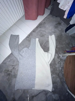 Tvåfärgad stickad tröja Gina Tricot - Säljer en ribbstickad tröja från Gina Tricot i storlek XS. Tröjan är delad i två färger, ljusgrå på ena sidan och offwhite på andra sidan. Den har lång ärm och hög hals, perfekt för kalla dagar. Supermjuk och trendig design!