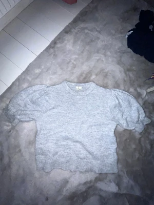 Grå puffärmad stickad tröja Gina Tricot - Mysig grå stickad tröja från Gina Tricot med puffärmar och rund halsringning. Tröjan har ribbstickade muddar vid ärmslut och nederkant, samt en något kortare och boxig passform. Perfekt för lager på lager och enkel att styla.