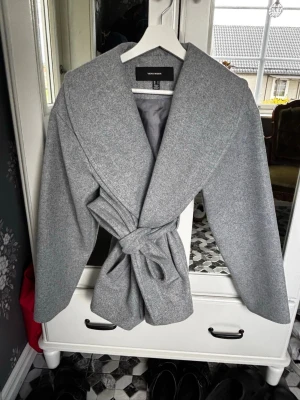 Grå kappa med knytskärp Vero Moda - Stilren grå kappa från Vero Moda med bred krage och knytskärp i midjan. Den är i väldigt fint skick och de enda är att den kan va lite nopprig där man haft väskan men annars inga fel. Sitter bra pp mig som brukar ha xs-s i vanliga kläder men storleken är M. 