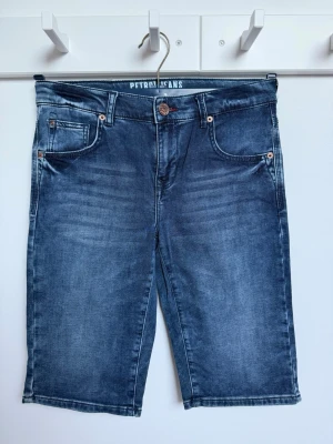 Blå jeansshorts från Petrol Industries  - Säljer ett par klassiska blå jeansshorts från Petrol Industries med fem fickor, knappgylf och bälteshällor. Shortsen har en normal passform och är tillverkade i slitstark bomull med snygga tvättade detaljer. Mycket bra skick, nyskick. Storlek 176/S