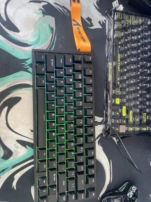 Kompakt mekaniskt tangentbord RGB - Säljer ett kompakt mekaniskt tangentbord med RGB-belysning och svart plastchassi. Tangentbordet har både Mac- och Win-läge som kan växlas på baksidan. Perfekt för gaming eller skrivande, med snygg grön bakgrundsbelysning på tangenterna.