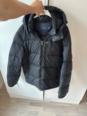 Svart Ralph lauren vinter dunjacka herr M - Svart glänsande eftertraktad och populär ursnygg vinter dunjacka av högsta kvalité och storlek M säljes. Inga hål eller fläckar och superfint skick så gott som ny! Nypris på nästan 6000 kr. Perfekta vinterjackan och superfint topp skick. Tveka inte vid minsta fråga eller fundering pris ej hugget i sten