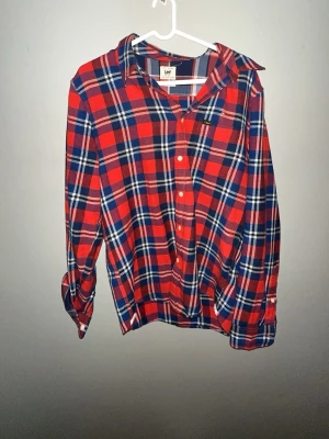 Röd och blå rutig skjorta från Lee - Klassisk rutig skjorta från Lee i rött, blått och vitt. Skjortan har långa ärmar, knappar framtill och en avslappnad passform. Perfekt för en casual look och enkel att styla med jeans 