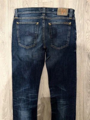 Nudie Jeans Tight Long John Mörkblå W31/L34 - Skinny Fit - Nudie Jeans Tight Long John ”Org. Calm Blues” mörkblå jeans med skinny fit-passform och låg midja, storlek W31/L34, midja 39 cm, ytterbenslängd 106,5 cm, benöppning 16,5 cm, modellen är 185cm & väger 65kg, i fint skick.
