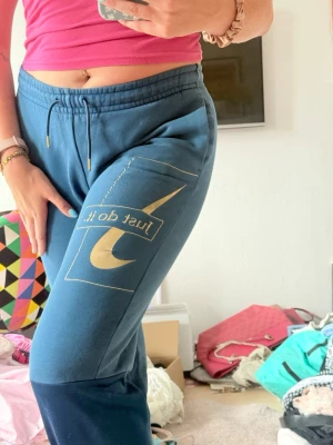 Blåa mjukisbyxor från Nike y2k - Snygga blåa mjukisbyxor från Nike med resår i midjan och avslappnad passform. Byxorna har sidofickor och är gjorda i ett mjukt, fleeceliknande material som känns skönt mot huden. Perfekta för chill dagar eller när du vill vara bekväm. Fin blå färg med guldigt tryck. Unika!! Y2k vibe