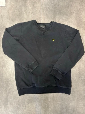Svart sweatshirt från Lyle & Scott - Säljer en svart sweatshirt från Lyle & Scott Junior med gul logga broderad på bröstet. Tröjan har rund halsringning, ribbade muddar vid ärmslut och nederkant samt klassisk passform. Perfekt för en avslappnad och stilren look.