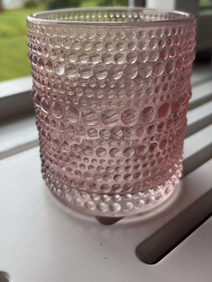 Rosa glas med bubbligt mönster - Säljer ett cylinderformat glas i ljusrosa glas med ett coolt bubbligt mönster runt hela ytan. Glaset är genomskinligt och har en unik struktur som gör det extra snyggt på bordet. Perfekt för dryck eller som dekoration.