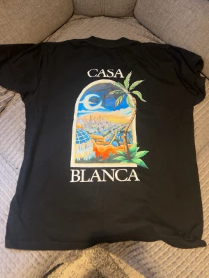 Svart Casablanca t-shirt med tryck - Snygg svart t-shirt med färgglatt tryck av ett fönster, palmer och stadsmotiv samt texten 'Casa Blanca' både fram och bak. T-shirten har rund hals och korta ärmar, perfekt för en avslappnad stil.