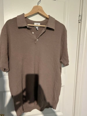 Beige pikétröja från H&M - Klassisk beige pikétröja från H&M i regular fit. Tröjan har korta ärmar, krage och knappar framtill. Materialet känns mjukt och strukturerat, perfekt för en avslappnad men ändå stilren look.